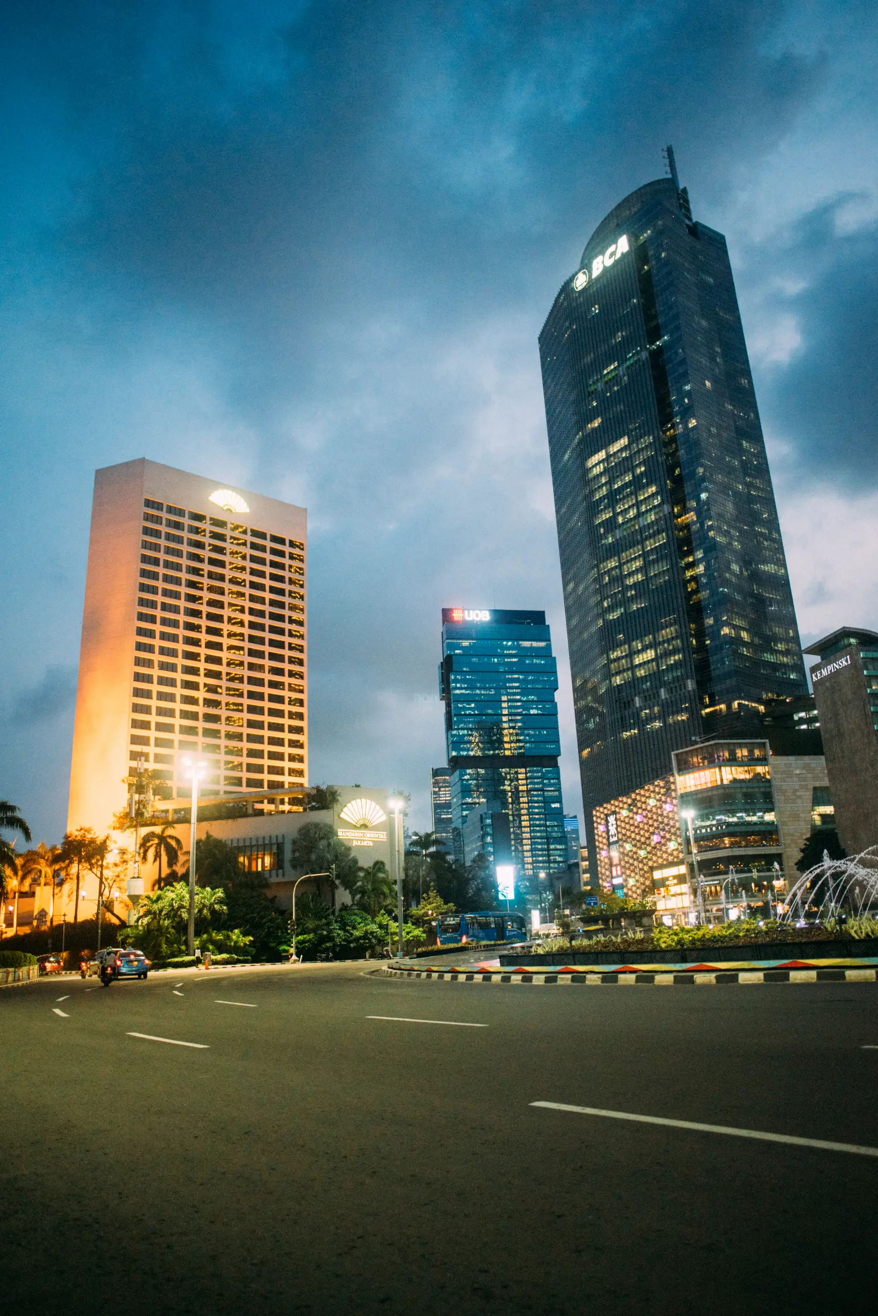 Downtown Jakarta skyline at dusk, featuring modern skyscrapers and vibrant city life with palm trees and lighted streets.