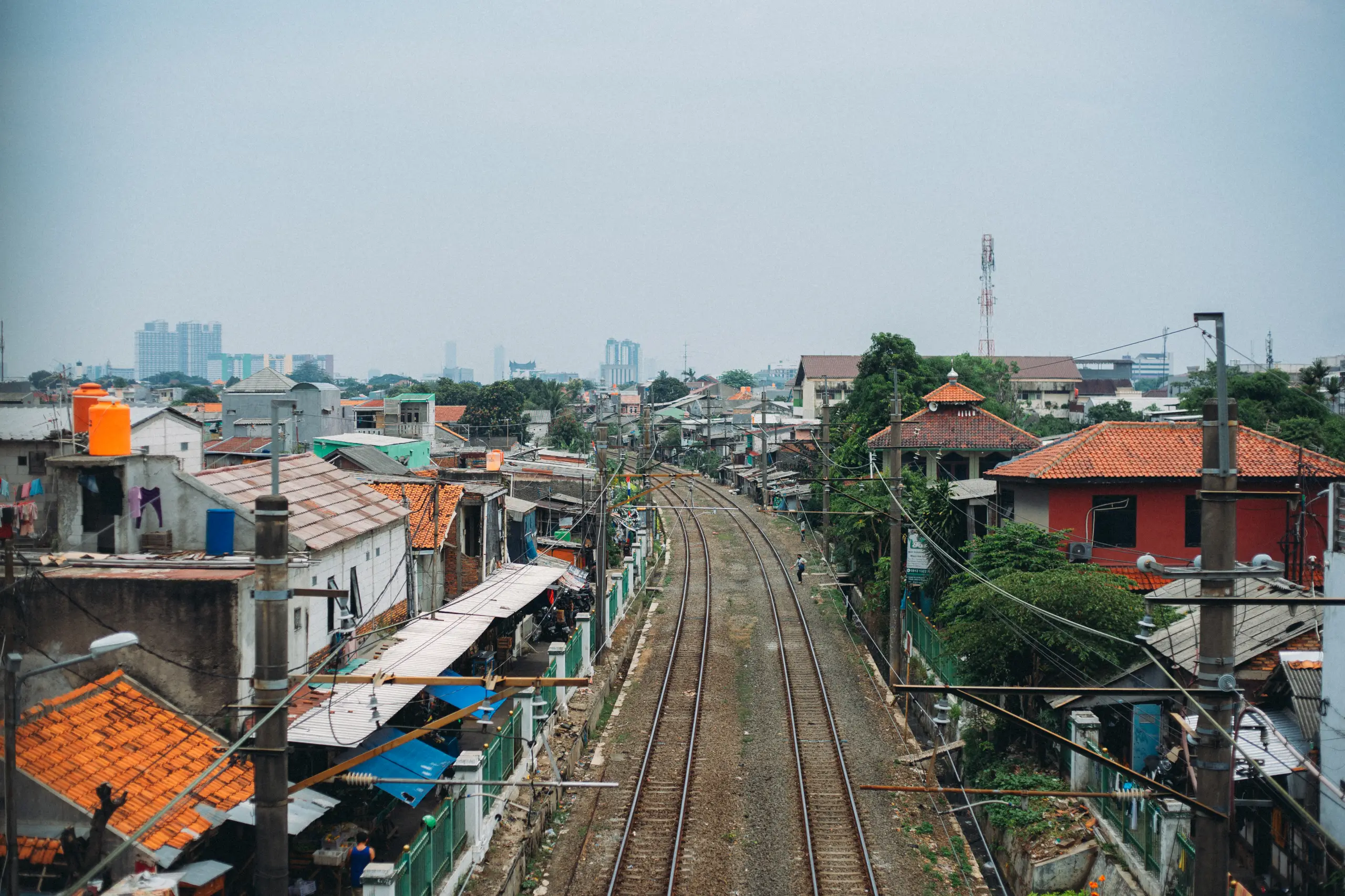 A view of a railway track flanked by colorful houses and buildings under a hazy sky, depicting urban life and infrastructure.